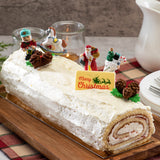 Bûche de Noël à la crème blanche décorée de figurines festives en plastique, Père Noël, casse-noisette et cheval à bascule.