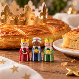 Trois fèves Rois Mages souriants en porcelaine de 3 cm devant une galette des rois dorée avec couronne, dans une ambiance festive d’Épiphanie.